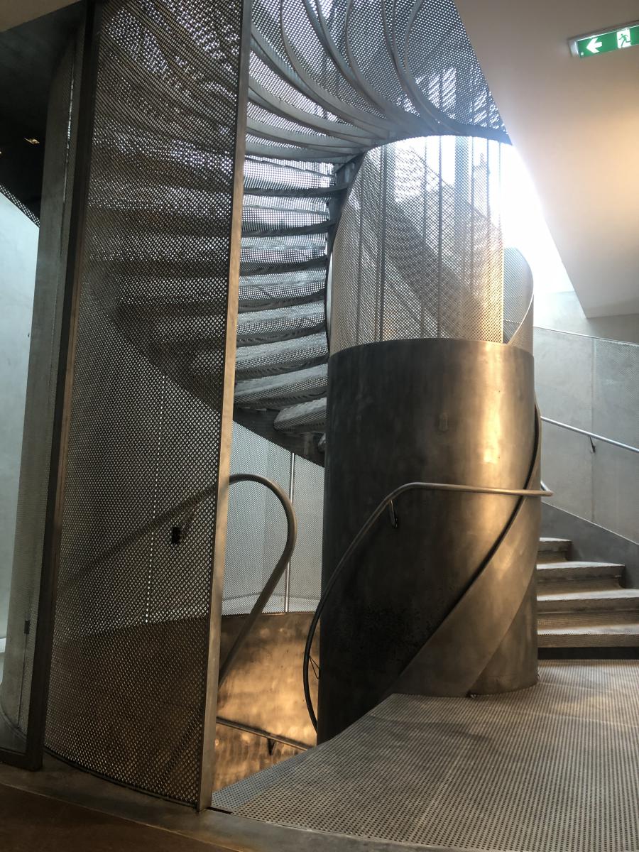 Escalier monumental en acier avec fût central en tôle roulée acier, garde-corps et marches en tôles perforées