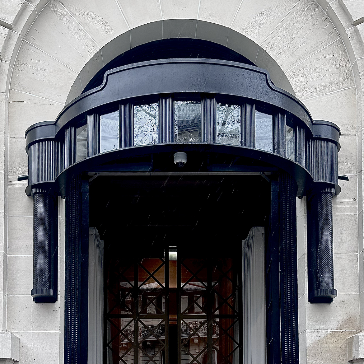 Marquise d’entrée en acier noir design sur bâtiment haussmannien Marquise d’entrée sur mesure en acier noir avec structure cintrée et vitrage, installée sur façade en pierre de style haussmannien
